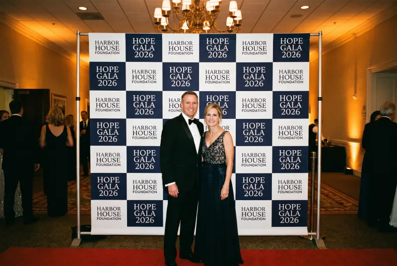 Couple posing at a charity gala in front of a navy and white step and repeat backdrop